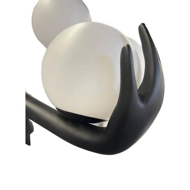 Close-up detail of black human sculpture floor lamp holding glowing orbs, showcasing intricate design