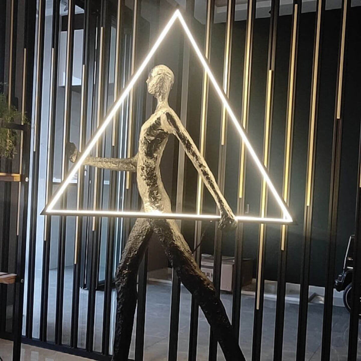 Side view of human statue floor lamp with geometric triangle design, illuminated with light on, casting warm ambient glow
