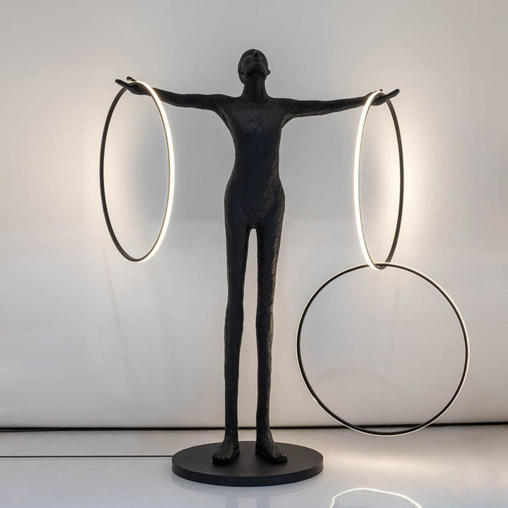 Human posing beside a burning circle LED floor lamp with warm light on, emphasizing the soft ambient glow and modern sculptural design