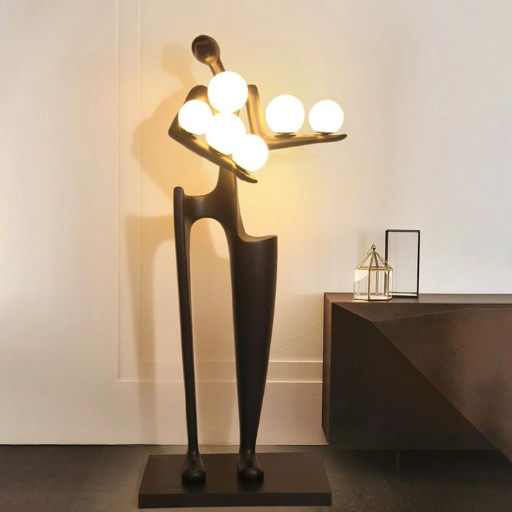 Dreamer black statue sculpture holding glowing globes, casting warm ambient light in a modern interior setting