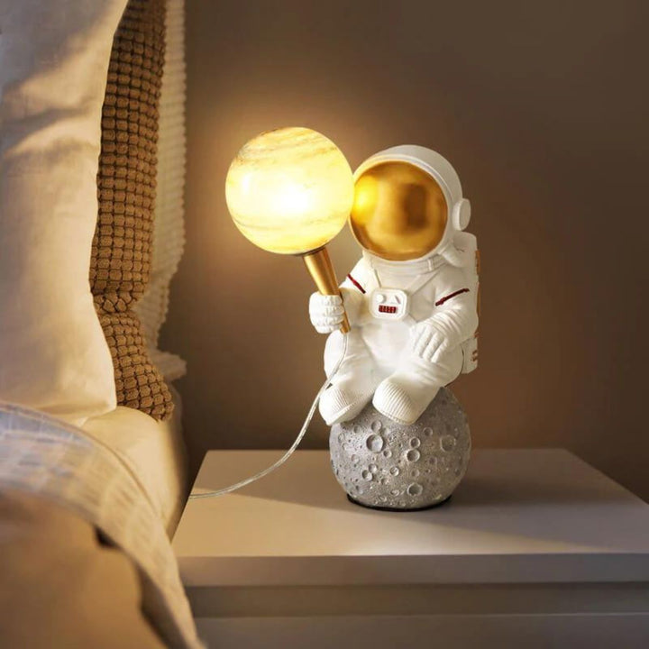 HTQ007 sitting astronaut table lamp with light on, placed beside bed in modern bedroom decor